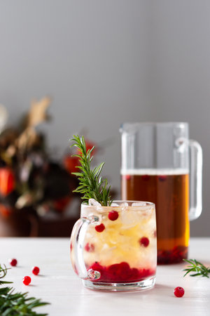 Cold refreshing black tea with ice and cranberries, jug and glass with berries and tea decorated with a sprig of rosemary on a white wooden backgroundの写真素材