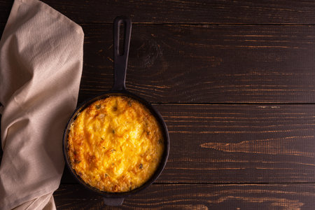 Frittata with cheese, mozzarella and stewed pumpkin in a cast iron pan on a wooden background