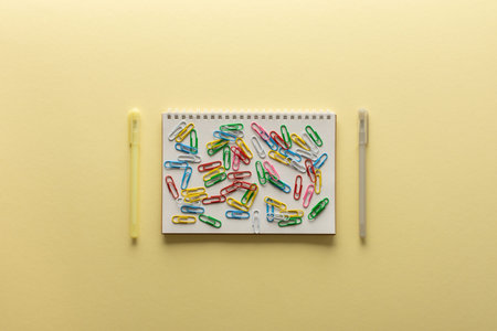 Open spiral notepad on yellow background , notebook lie on paper,paper clips of different colors on...