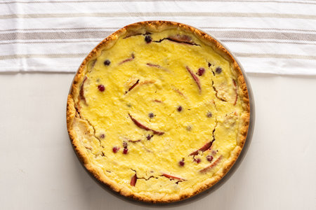 Delicious sweet cheese pie with apples and cranberries, fruit and berry curd pie on a white background with a kitchen towel, top viewの写真素材