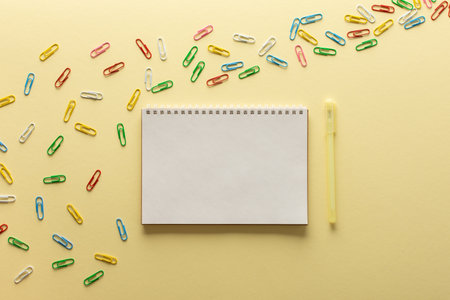 Open spiral notepad on yellow background , notebook and pen lie on textural paper, flat lay concept in trendy colors of the year, paper clips of different colorsの写真素材