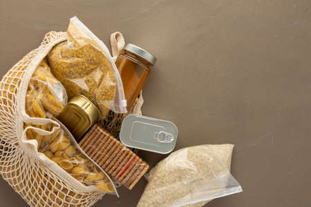 Home food supplies, necessary food for the period of quarantine and isolation, the concept of stay at home, eco bag with assorted pasta, rice and bulgur, cookies, canned food and honey,top viewの写真素材