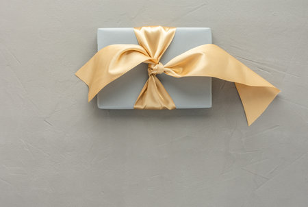 Gray gift box with golden bow on a gray concrete background, birthday or valentine concept, top view, copy spaceの写真素材