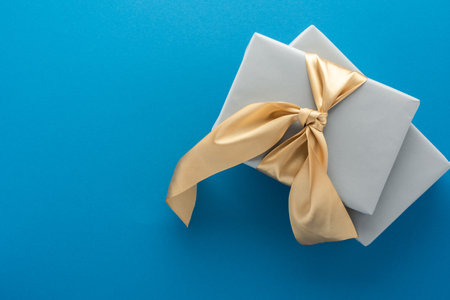 Gray gift boxes with golden bow on a blue background, birthday or valentine concept, top view, copy spaceの写真素材