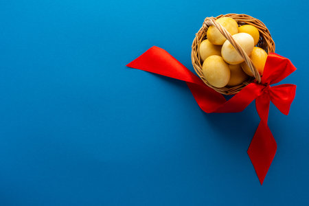 Easter yellow painted eggs in a basket and red ribbon on bright blue background, easter festive conceptの写真素材