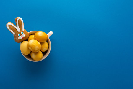 Easter yellow painted eggs and biscuits bunny in a mug on bright blue background, easter festive conceptの写真素材
