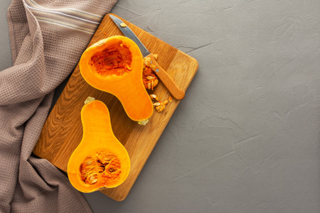 Raw organic butternut pumpkin or gramma cut in half close-up on wooden board with knife and kitchen towel on gray concrete background, top view, copy spaseの写真素材