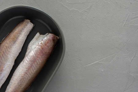 Two raw hake carcasses in a ceramic bowl on grayの写真素材