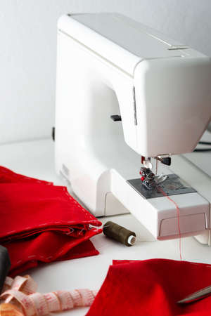 Modern sewing machine with red and gray fabric, measuring tape and thread, cutting and sewing at home, home leisure and hobbyの写真素材