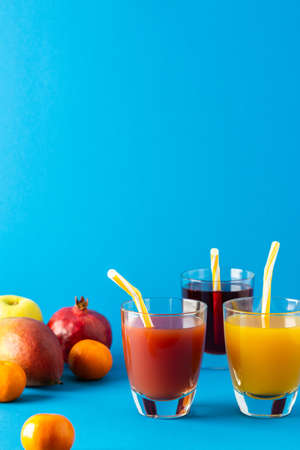 Delicious sweet citrus, mango and pomegranate juices in glasses and ripe fruits on a blue backgroundの写真素材