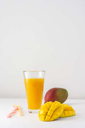 Mango juice in glasses with juice and a straw on a white background, chopped mango and whole, delicious healthy sweet natural drinkの写真素材