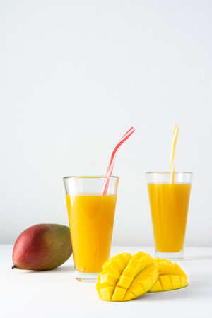 Mango juice in glasses with juice and a straw on a white background, chopped mango and whole, delicious healthy sweet natural drinkの写真素材