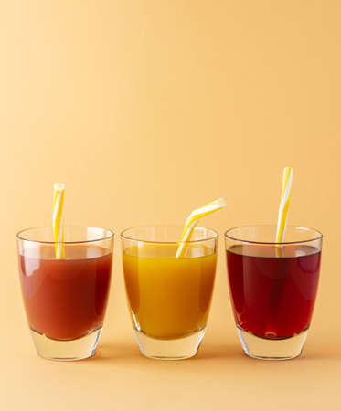 Delicious sweet citrus, mango and pomegranate juices in glasses with a straw isolated on beige backgroundの写真素材