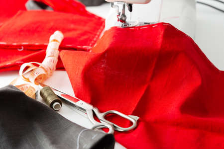 Modern sewing machine with red and gray fabric, measuring tape and thread and scissors, cutting and sewing at home, domestic leisure and hobbyの写真素材