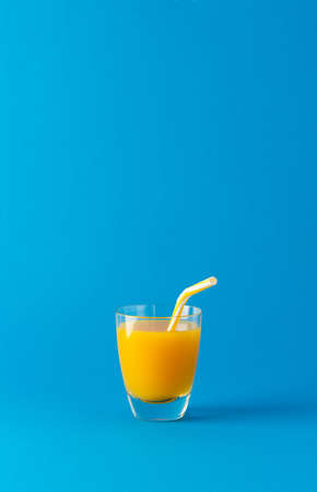 Delicious sweet orange or mango juice in glass with a straw isolated on blue backgroundの写真素材