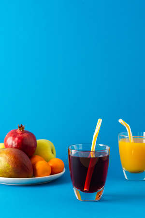 Delicious sweet citrus, mango and pomegranate juices in glasses and ripe fruits on a blue backgroundの写真素材