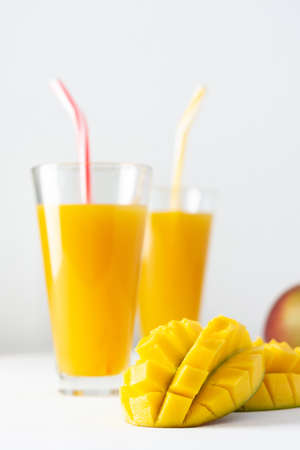 Mango juice in glasses with juice and a straw on a white background, chopped mango and whole, delicious healthy sweet natural drinkの写真素材