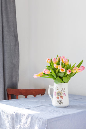 Beautiful spring bouquet of pink tulips in a jug on the table, flowers in a home interior