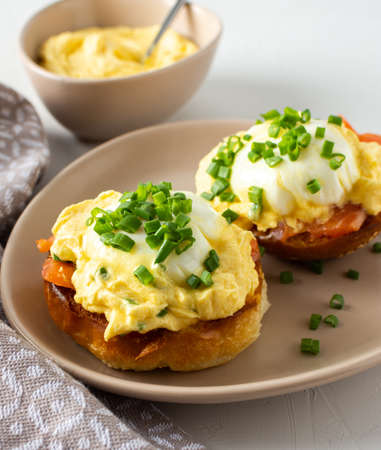 Delicious hearty breakfast, eggs Atlantic in a plate on a white background, round fried bun with salmon and eggs Benedict, hollandaise sauce and green onionsの写真素材