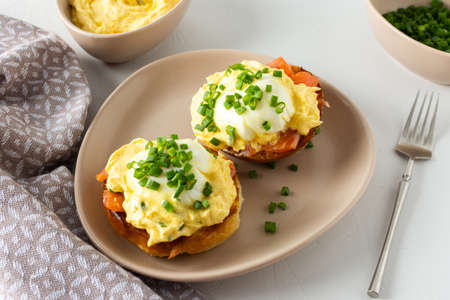 Delicious hearty breakfast, eggs Atlantic in a plate on a white background, round fried bun with salmon and eggs Benedict, hollandaise sauce and green onionsの写真素材