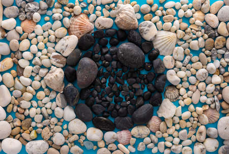 Sea light pebbles and shells on a blue background, in the middle of a circle of dark pebbles, vacation on the sea or oceanの写真素材