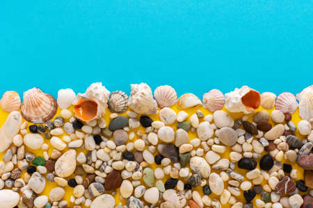 Sea light pebbles and shells on a blue and yellow background, copy space, vacation on the sea or ocean, background like sand with waterの写真素材
