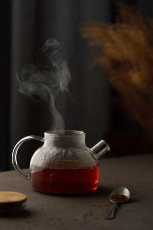 The process of brewing rooibos tea with herbs, glass teapot with caffeine free tea drenched in boiling water, the steam rises above the teapotの写真素材