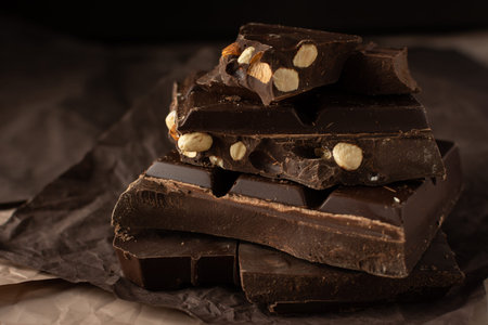 Dark chocolate with almonds and hazelnuts in a stack on brown background