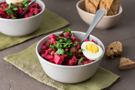 Russian salad vinaigrette in plates with boiled egg and black bread, salad of boiled potatoes and carrots, beetroot and pickled vegetables, cucumber and cabbage and canned green peasの写真素材