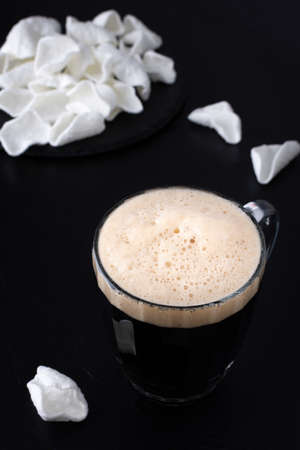 Dark craft beer with foam in a mug with white potato chips on black backgroundの写真素材