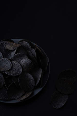 Black crispy potato chips scattered on black backgroundの写真素材