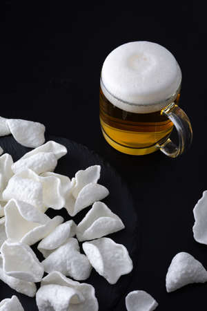Glass with light beer in a mug with white potato chips on black backgroundの写真素材