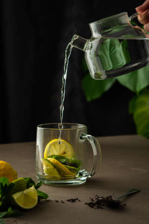 Woman pours boiling water from a teapot into a mug with mint, lemon, lime and black tea, tea brewing processの写真素材