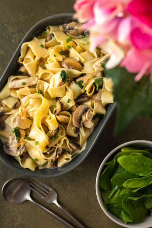 Fettuccini pasta with mushrooms and chicken breast and basil in a creamy sauce, top view, a vase of flowers on the tableの写真素材