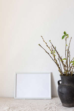 Home decor mock-up, blank picture frame near white painted concrete wall , black earthenware jug with pussy willow branches and blossoming green leavesの写真素材