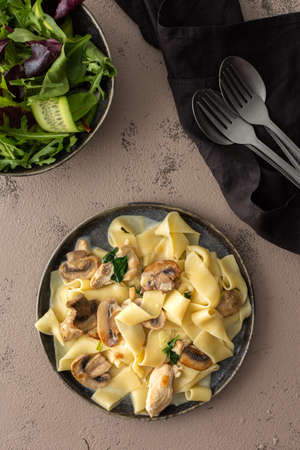 Fettuccini pasta with mushrooms and chicken breast and basil in a creamy sauce, top view, green fresh mix saladの写真素材