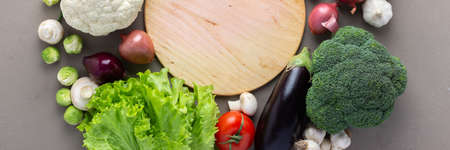 Fresh farm organic vegetables banner, healthy food concept, vegetables and mushrooms around a round cutting board on a gray background, top view, copy spaceの写真素材