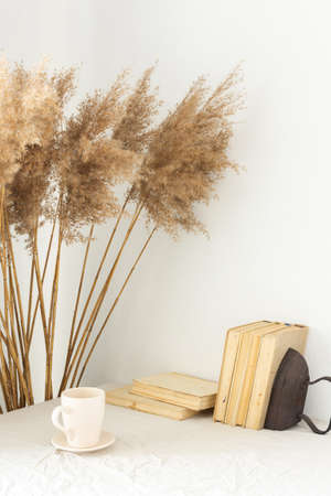 Home decor , blank picture frame near white painted concrete wall , dry Cane Reeds and old books, a cup of coffeeの写真素材