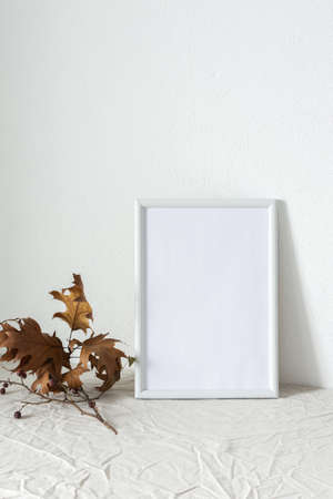 Home decor mocap, empty picture frame near white painted concrete wall, branches with dry leavesの写真素材