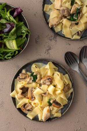 Fettuccini pasta with mushrooms and chicken breast and basil in a creamy sauce, top view, green fresh mix saladの写真素材