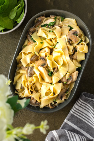 Fettuccini pasta with mushrooms and chicken breast and basil in a creamy sauce, top view, a vase of flowers on the tableの写真素材