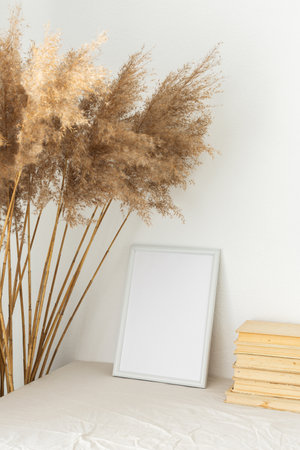 Home decor mock-up, blank picture frame near white painted concrete wall , dry Cane Reeds and old booksの写真素材