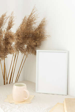 Home decor mock-up, blank picture frame near white painted concrete wall , dry Cane Reeds and old books, a cup of coffeeの写真素材