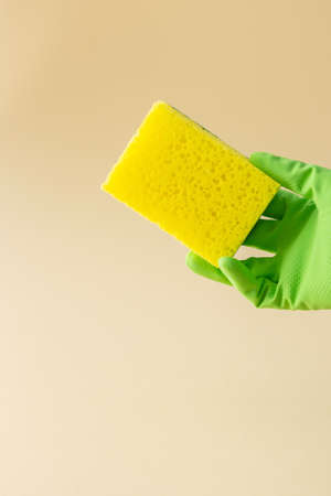 Hand in green rubber glove holds yellow dishwashing sponge, cleaning conceptの写真素材