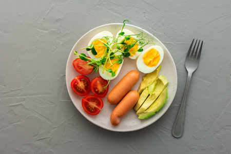 Delicious breakfast, boiled eggs with sausages, tomatoes and avocado, microgreens of peas and...