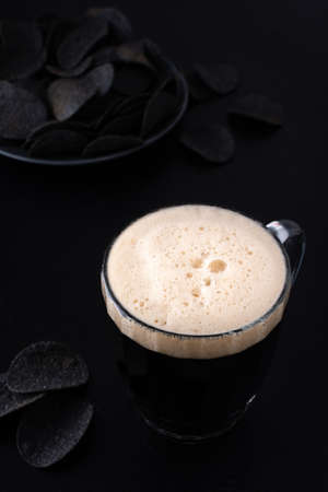 Dark craft beer with foam in a mug with black potato chips on dark backgroundの写真素材