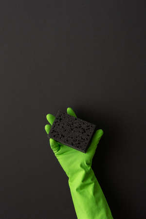 A hand in a green protective rubber glove holds a black washing sponge on a black backgroundの写真素材