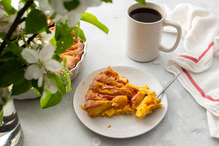 Piece of apple pie on a plate with a spoon, cut pie in a round baking dish, flowering branches of an apple treeの写真素材