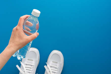 Female hand with a bottle of water, white sneakers on the floor, doing sports and training in the gym, active healthy lifestyle, top view, copy spaceの写真素材