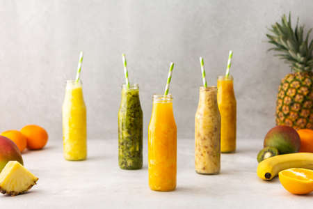 Fruit smoothies in jars with straws, pineapple and kiwi fruits on the sides, banana and mango with orangeの写真素材